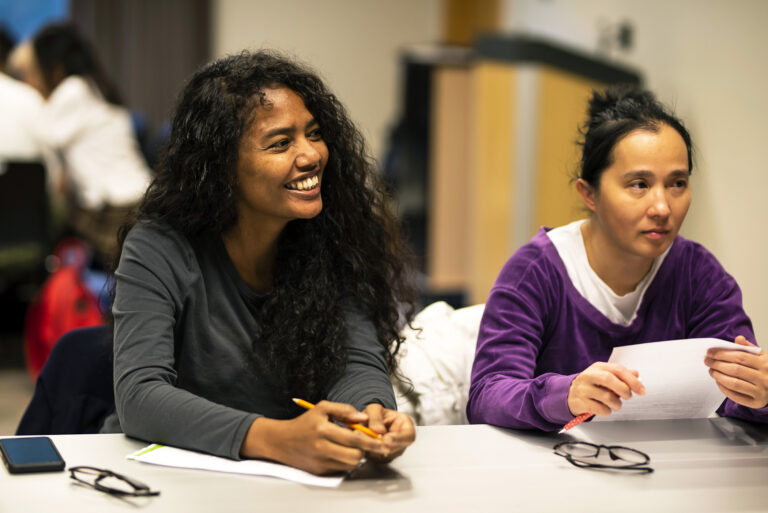 Participants at a an english language learning class smile as they sit around a table.