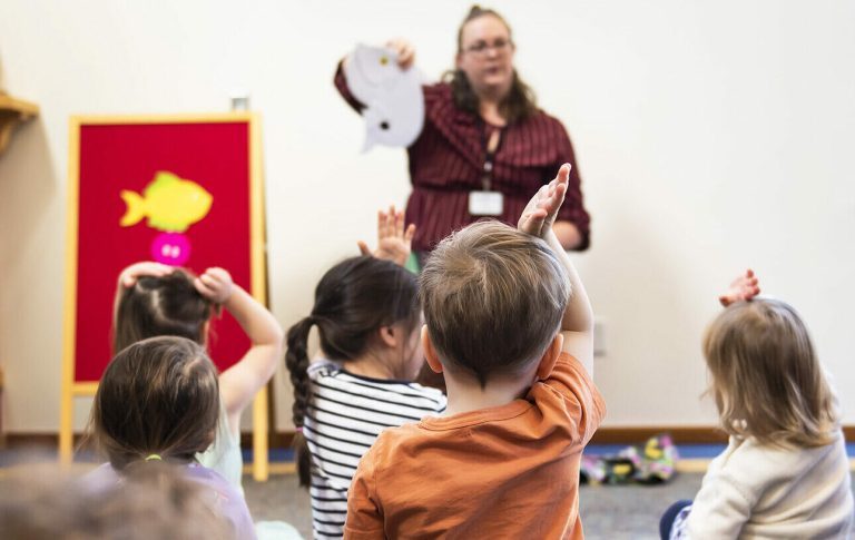 A youth librarian holds up a felt animal in front of a group of kids sitting during storytime.