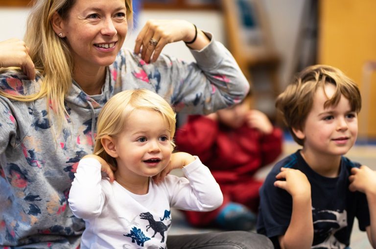 A parent and two children smile with their hands on their shoulders.