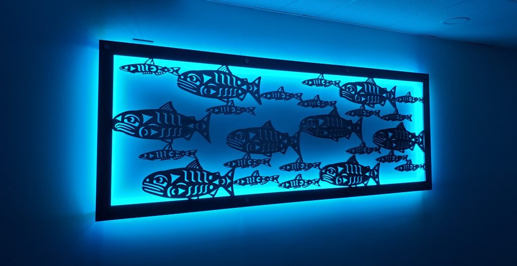 aluminum art panel of cut-out coast salish salmon designs illuminated from behind with blue LED lights around edge