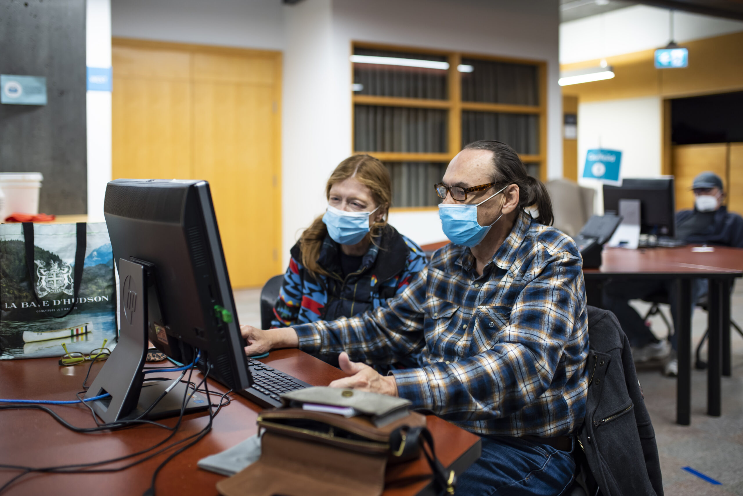 A pair of people using masks sits at a computer in the community computing centre.