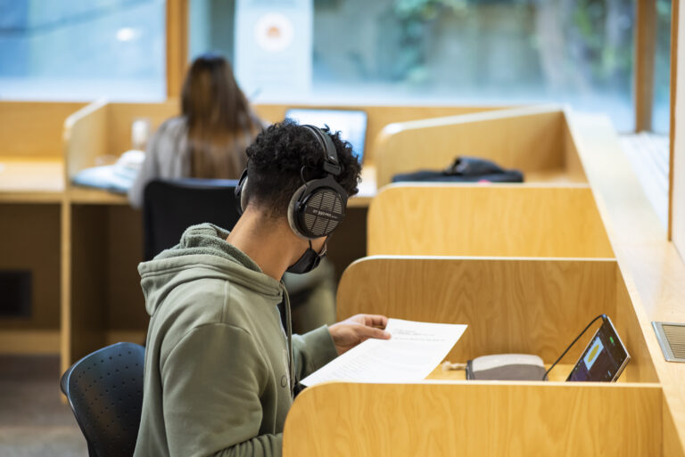 A person with headphones sits at a study carrel