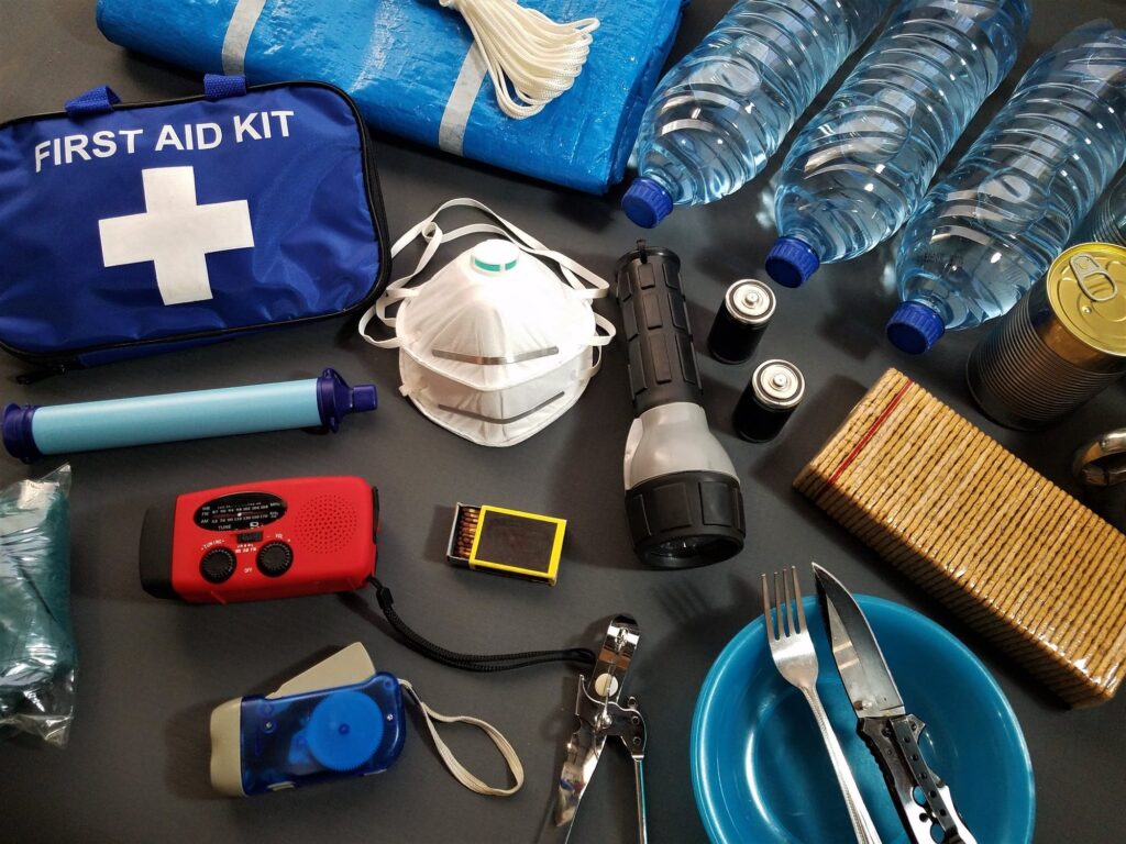 A bird's-eye view of various emergency kit items, like first aid kit, N95 mask, bottled water, on a table,.