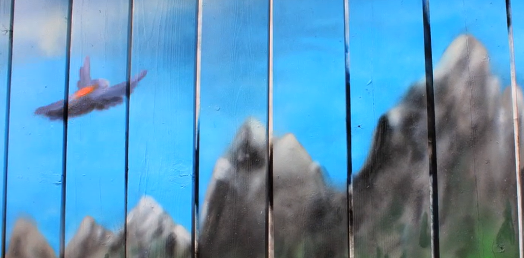 Spray painted fence with a blue sky, mountains and flying bluebird.