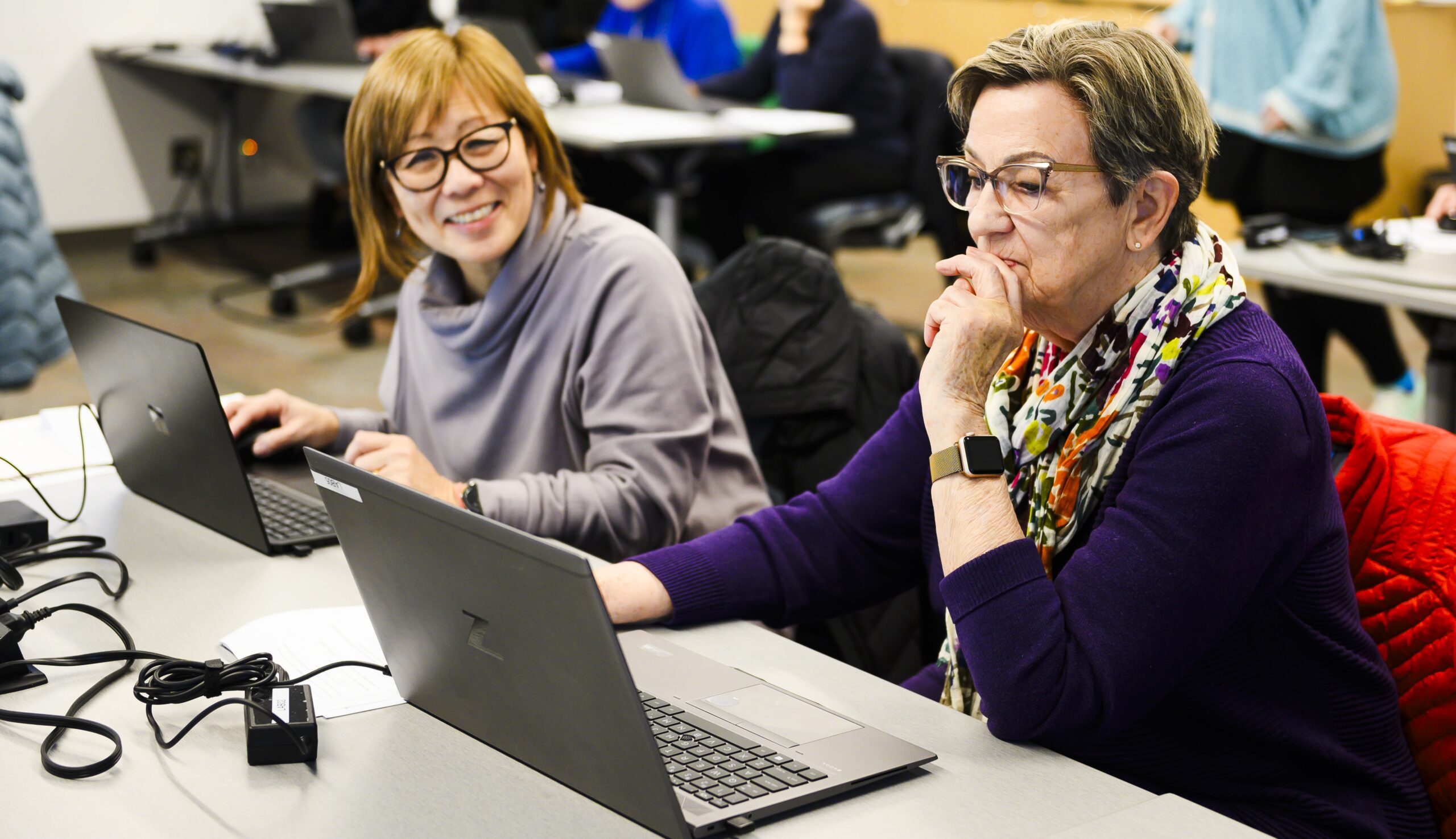 two adult learners sit in front of laptops in the lab