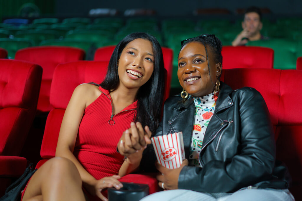 two women lean in to each other as they watch a movie in a cinema