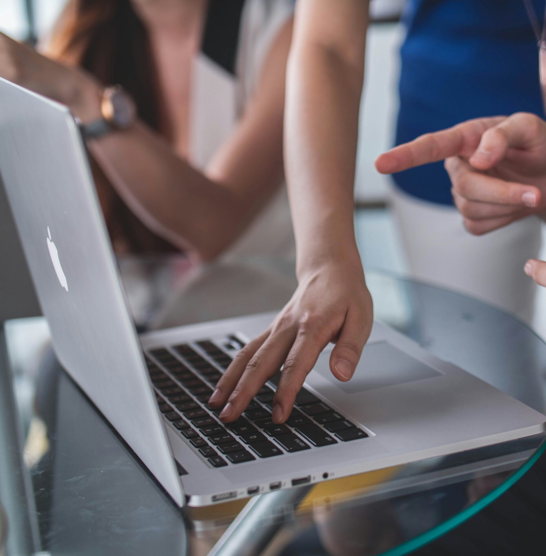 Two sets of hands pointing at and using a MacBook.