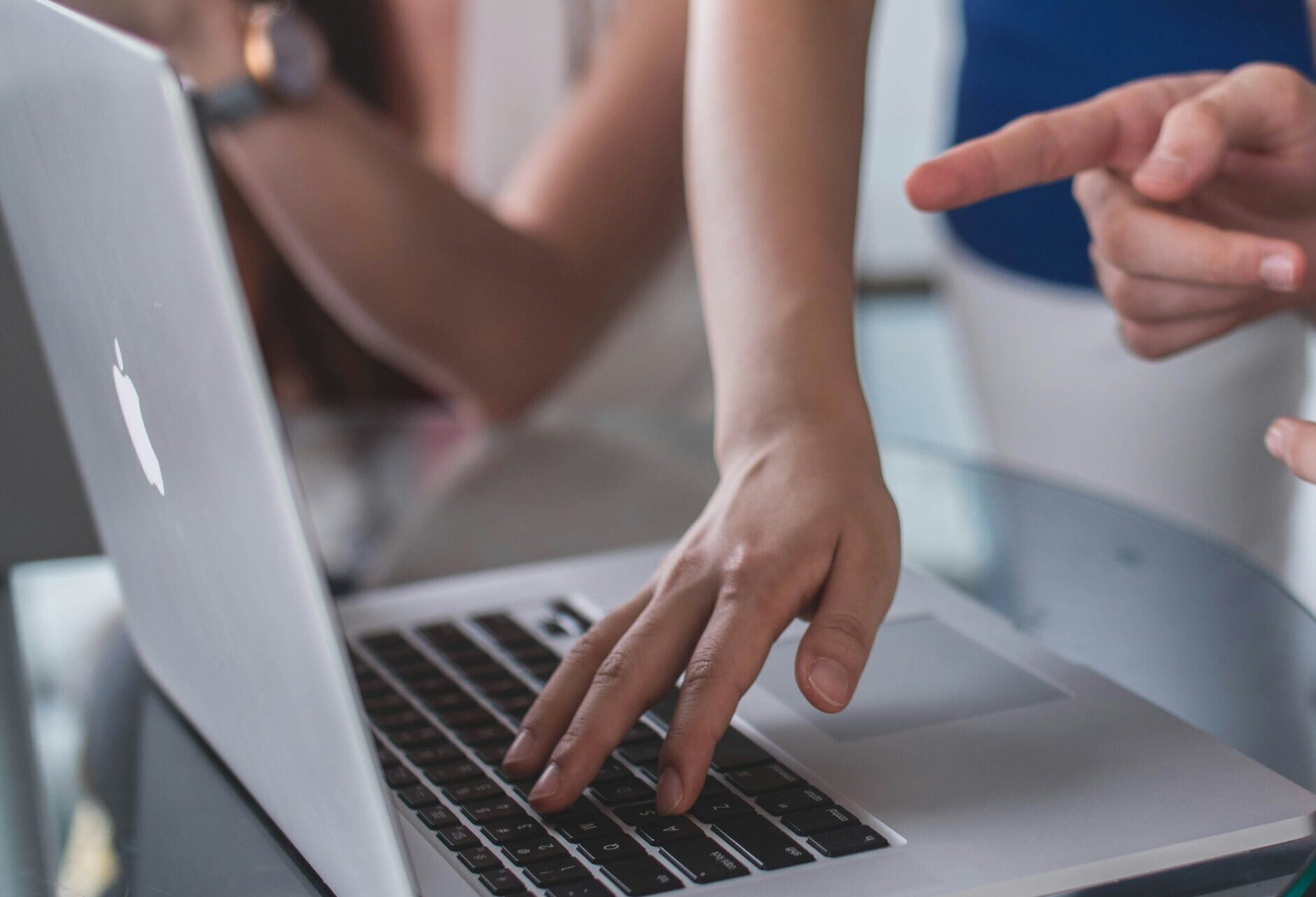 Two sets of hands pointing at and using a MacBook.