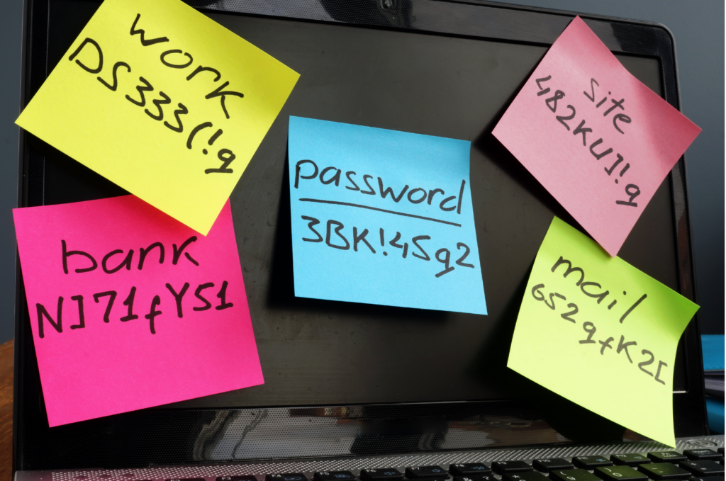 Passwords written on sticky notes attached to a laptop screen.