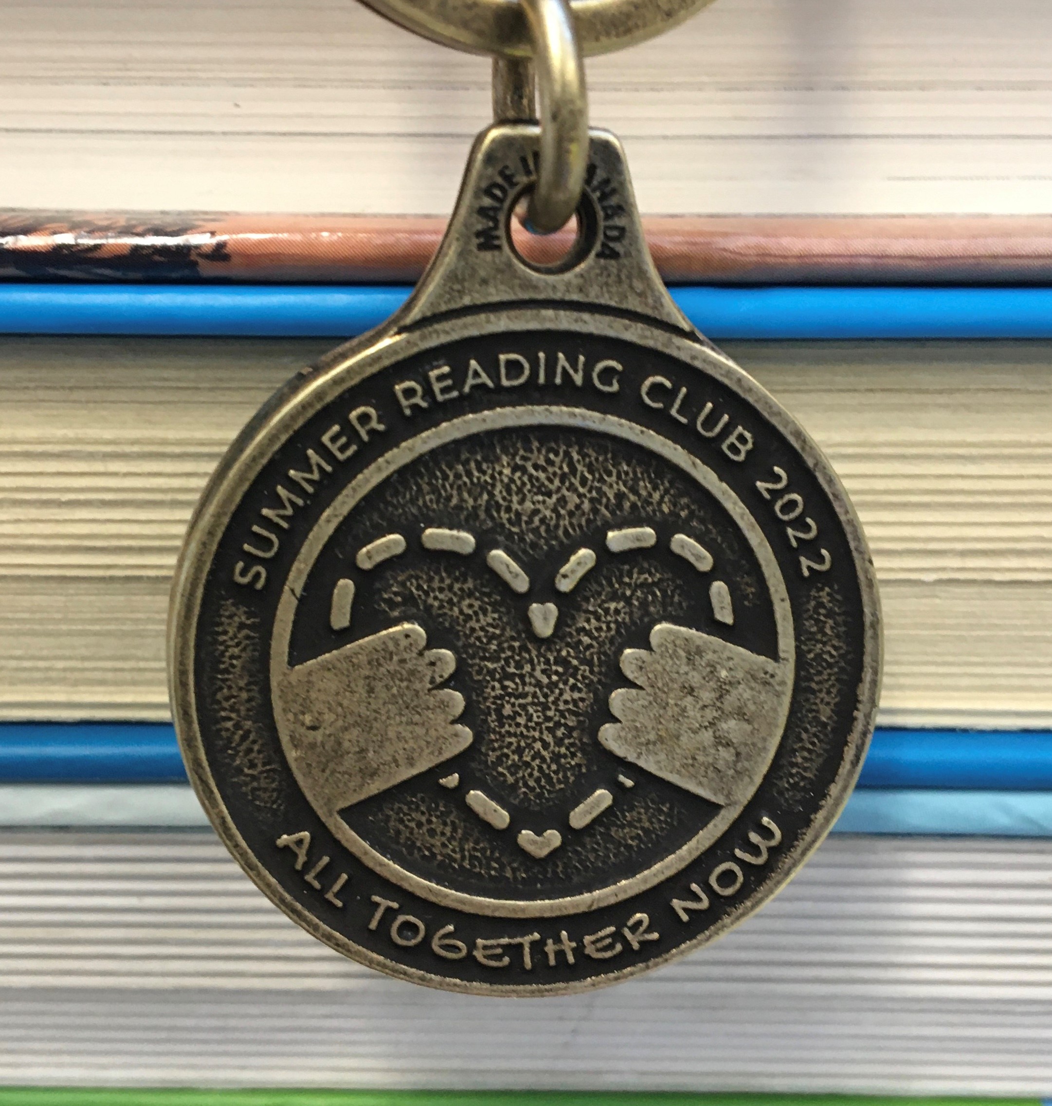 A past year's Summer Reading Club Medal hangs in front of a pile of books.