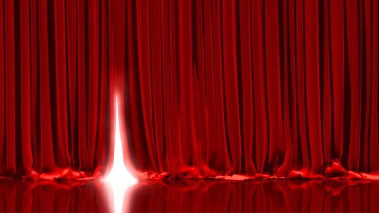 Light shining behind a red stage curtain.