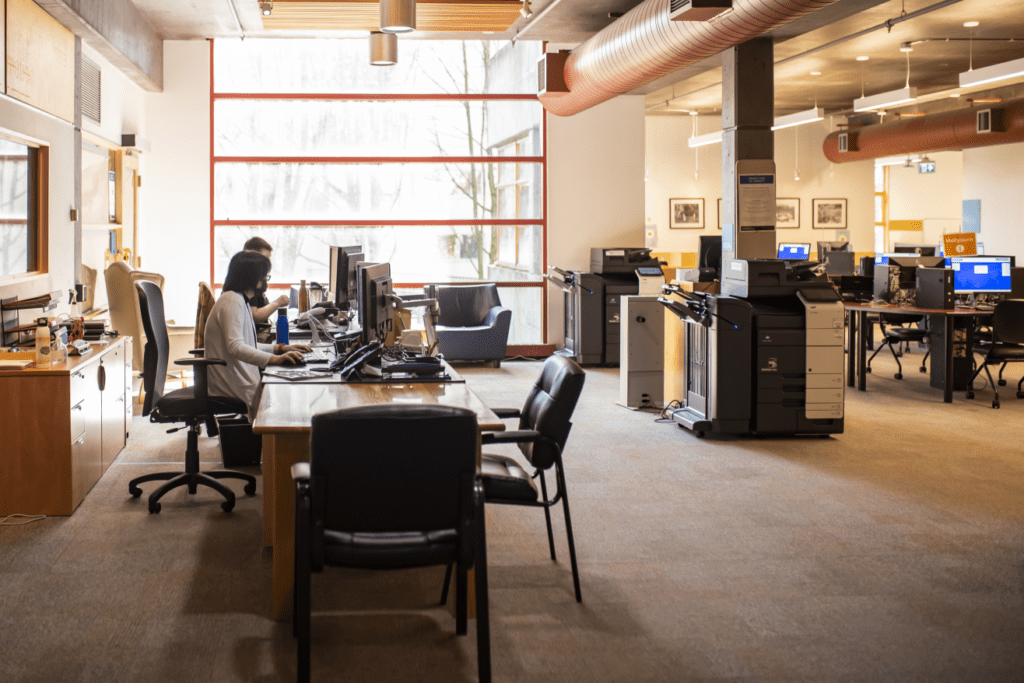 Two staff sit at the help desk in the Community Computing Centre in front of public computer stations, photocopier, and printer stations.