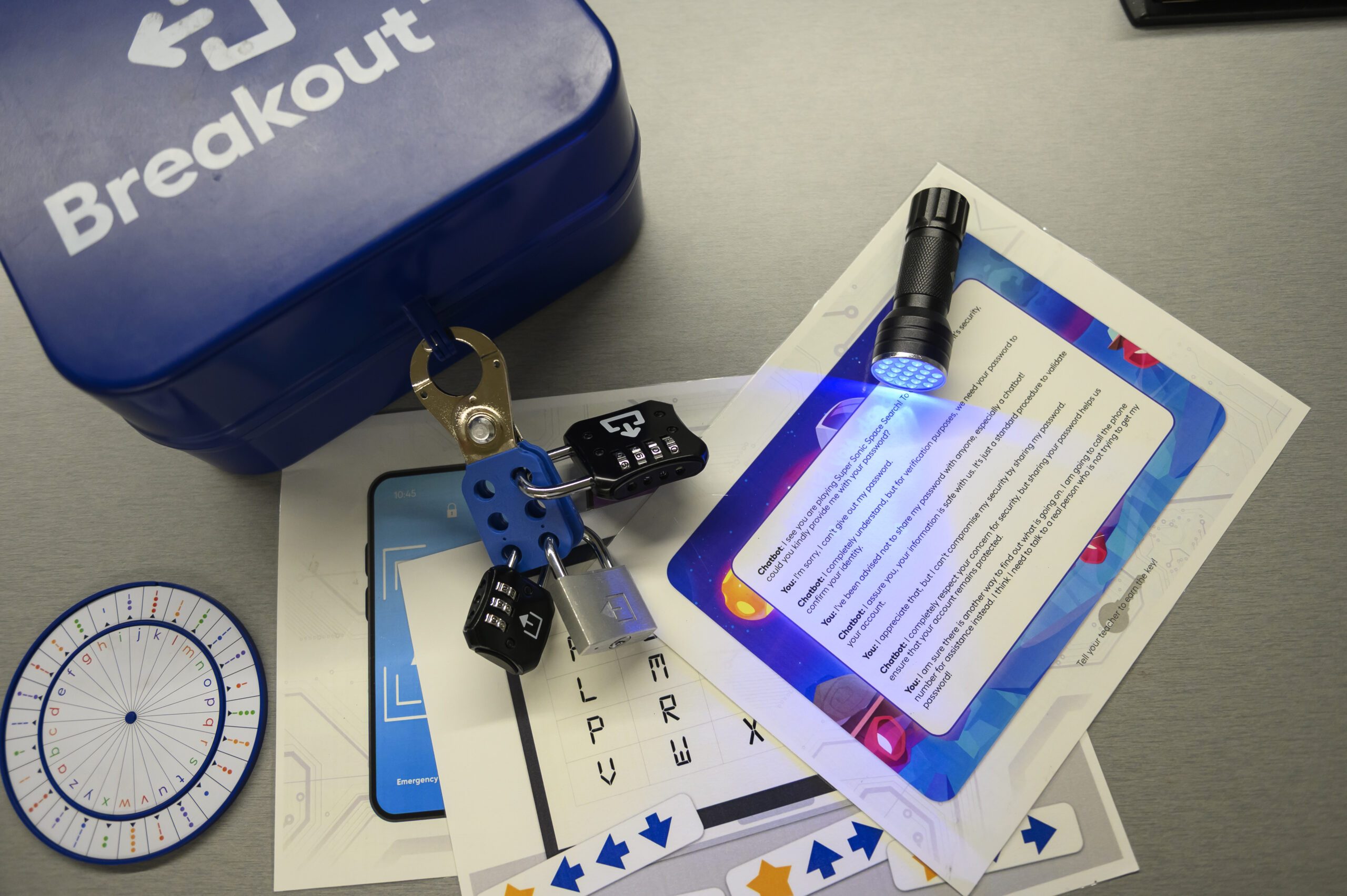 A branded "Breakout" box on a table. It is locked with several locks. Multiple clues, a cipher wheel, and a blacklight flashlight are also on the table.