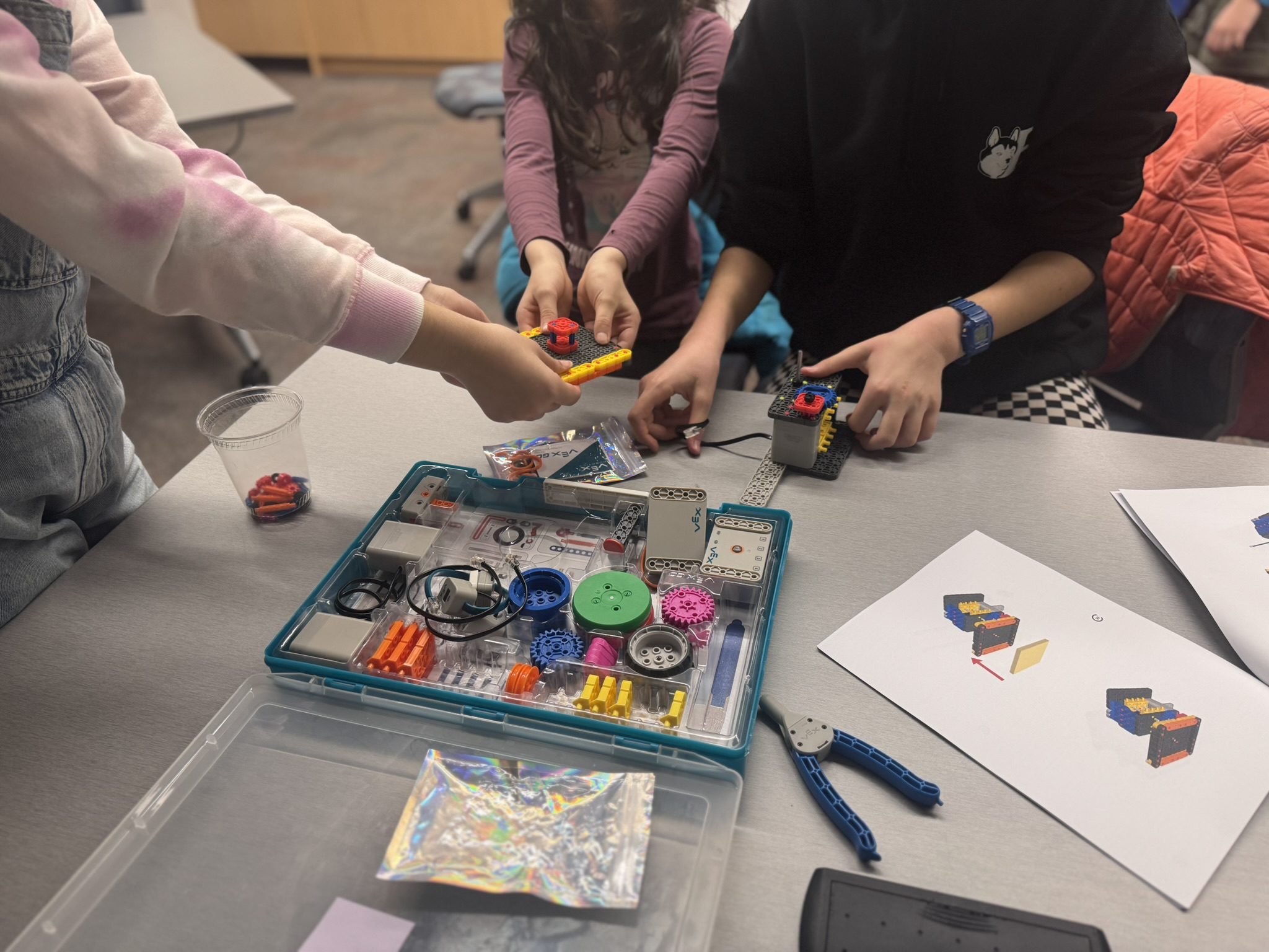 Three kids build a robot together with colourful robotics pieces.