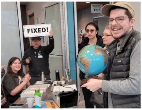 Volunteers for a repair cafe. One is holding up a sign that says FIXED.