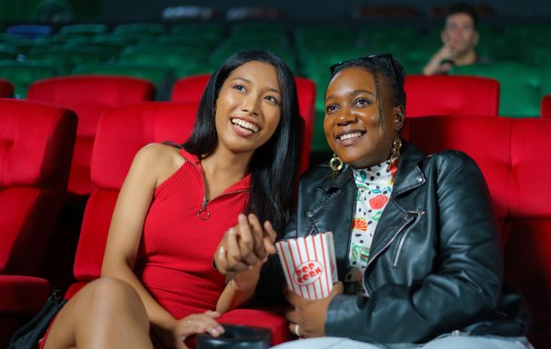 two women lean in to each other as they watch a movie in a cinema
