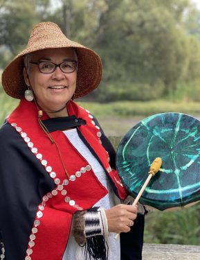 Kung Jaadee plays a hand drum in front of a lake
