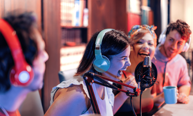 Four adults wearing headphones laugh.