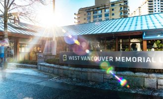 A beam of sunlight crosses the exterior of the Library building. The sign out front reads "West Vancouver Memorial"