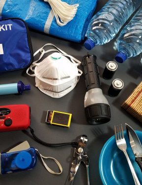 A bird's-eye view of various emergency kit items, like first aid kit, N95 mask, bottled water, on a table,.