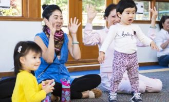 A group of adults and small children dance, clap, and sing at storytime.