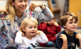 A parent and two children smile with their hands on their shoulders.