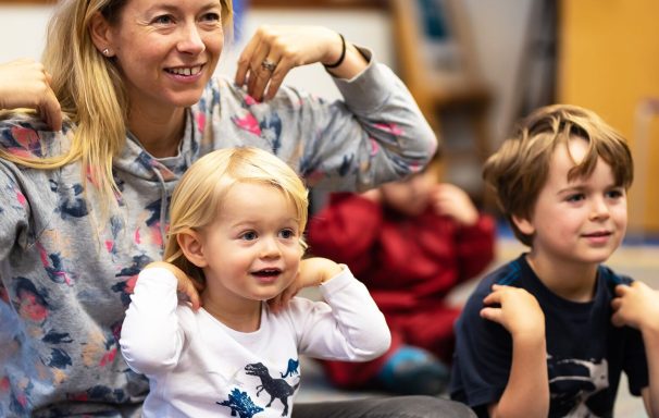 A parent and two children smile with their hands on their shoulders.